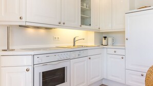 Una cocina moderna con armarios blancos, un lavamanos de acero inoxidable, horno empotrado y cafetera.