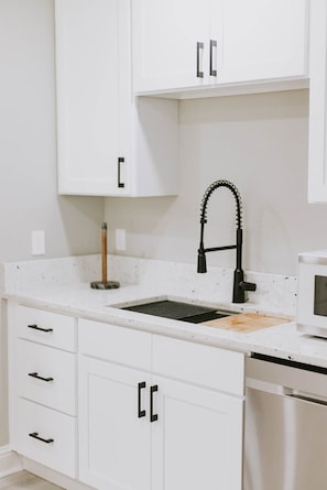 A kitchen with white cabinets, a black faucet, and a microwave.