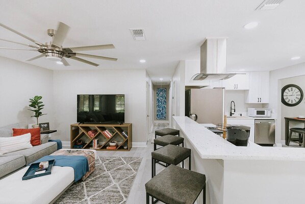 A modern living room with a TV, sofa, and a dining area with bar stools.
