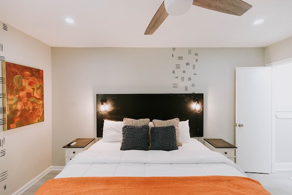 A modern bedroom with a large bed, two bedside tables, a ceiling fan, and a wall-mounted light fixture.