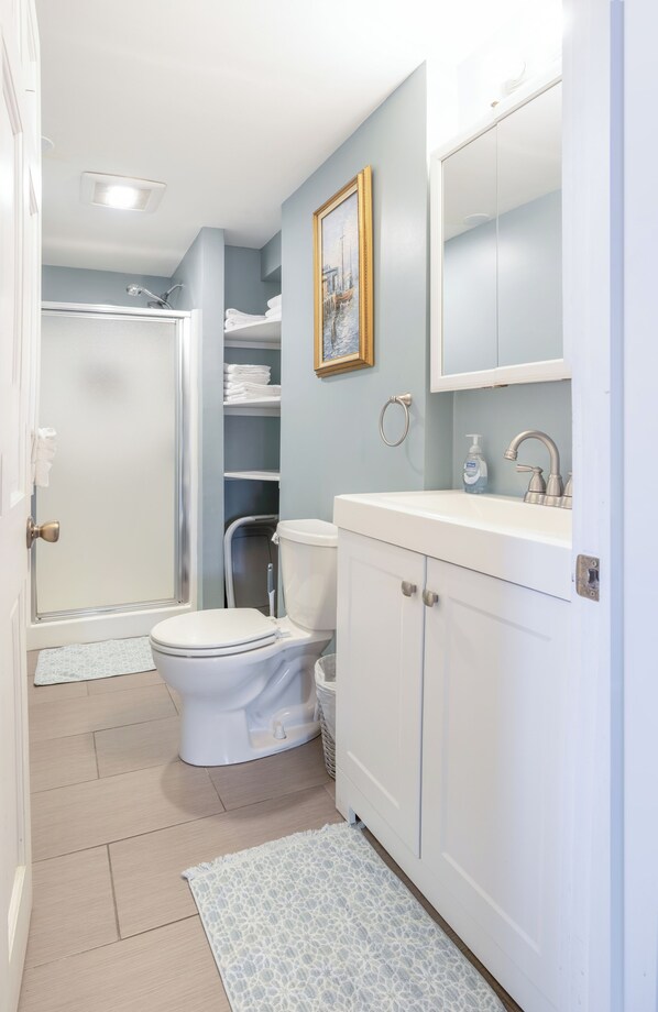 A bathroom with a toilet, sink, and shower. There is a towel rack and a framed picture on the wall.