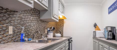 Una cocina con salpicadero de azulejos, un fregadero, armarios, un microondas y una cafetera.