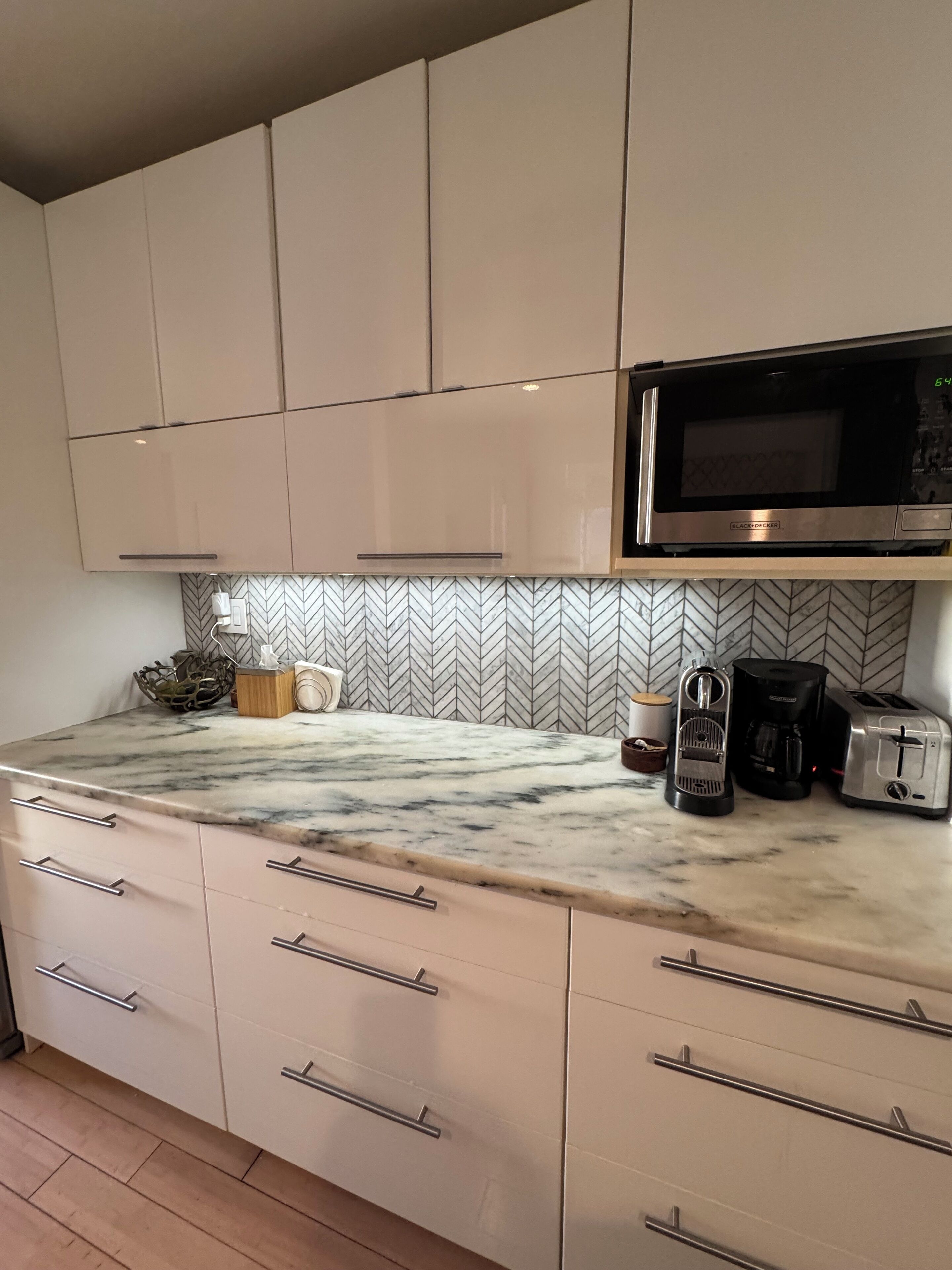 A kitchen with beige cabinets, a marble countertop, a microwave, a coffee maker, and a toaster.