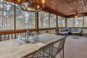 A covered outdoor deck with a wooden table, metal chairs, a cushioned seating area, and large windows. - The Mason Jar At Ellijay | Ellijay, GA (Ellijay)
