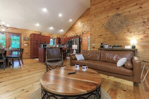 A cozy cabin interior with a wooden dining area, a leather sofa, and a kitchen with wooden cabinets.