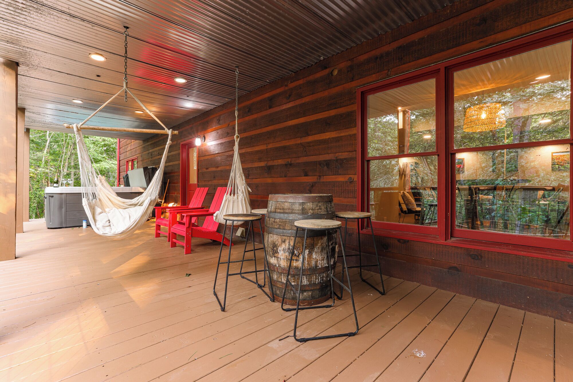 A wooden deck with a hammock, red chairs, and a barrel stool.