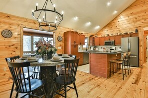L’intérieur d’un chalet en bois comprend une table à manger, des chaises, un lustre, des appareils de cuisine et une grande fenêtre.