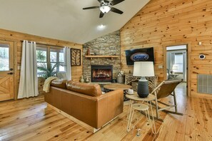 L’intérieur d’un chalet en bois, avec une cheminée, un canapé en cuir, une table à manger et un ventilateur de plafond.
