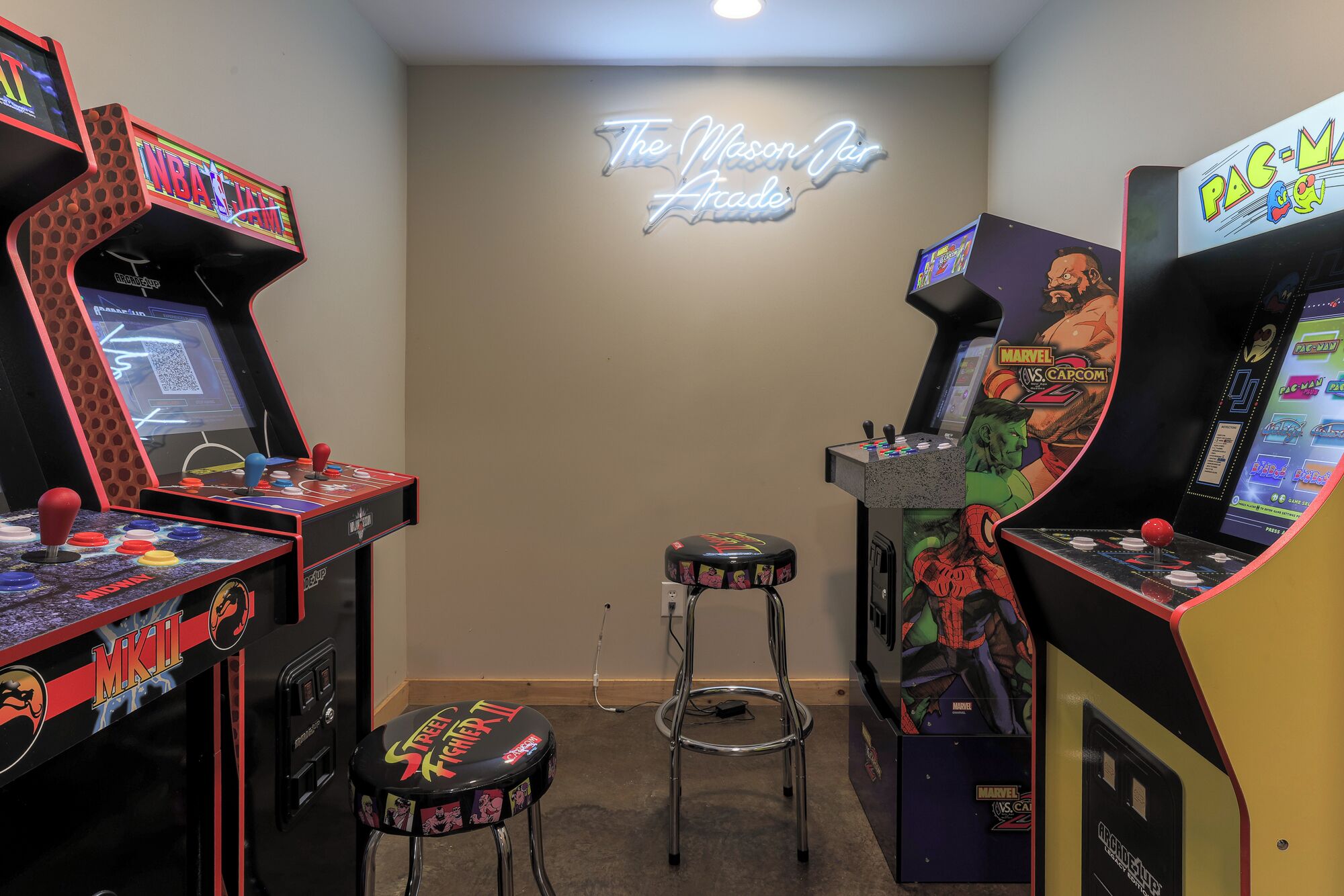 A room with arcade gaming machines, including NBA Jam and Marvel vs. Capcom 2, and a neon sign reading 'The Moon Jar Arcade'.