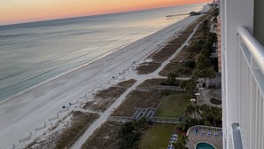 A beach view from a balcony with a clear sky, a sandy beach, a pier, and a pool area.