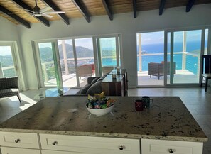 Une cuisine spacieuse dotée d’un grand  îlot central, d’un ventilateur de plafond et offrant une vue sur l’océan grâce à de grandes fenêtres.