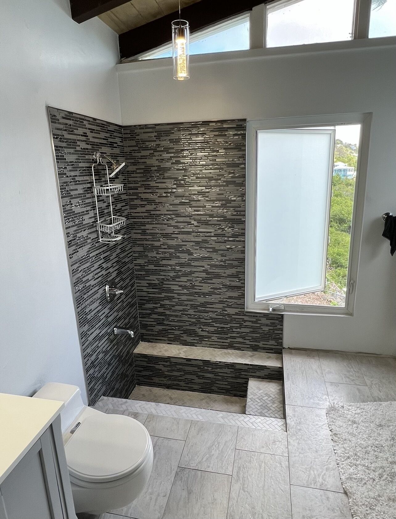 Et moderne badeværelse med stenvæg, bruser, toilet og et vindue med udsigt.