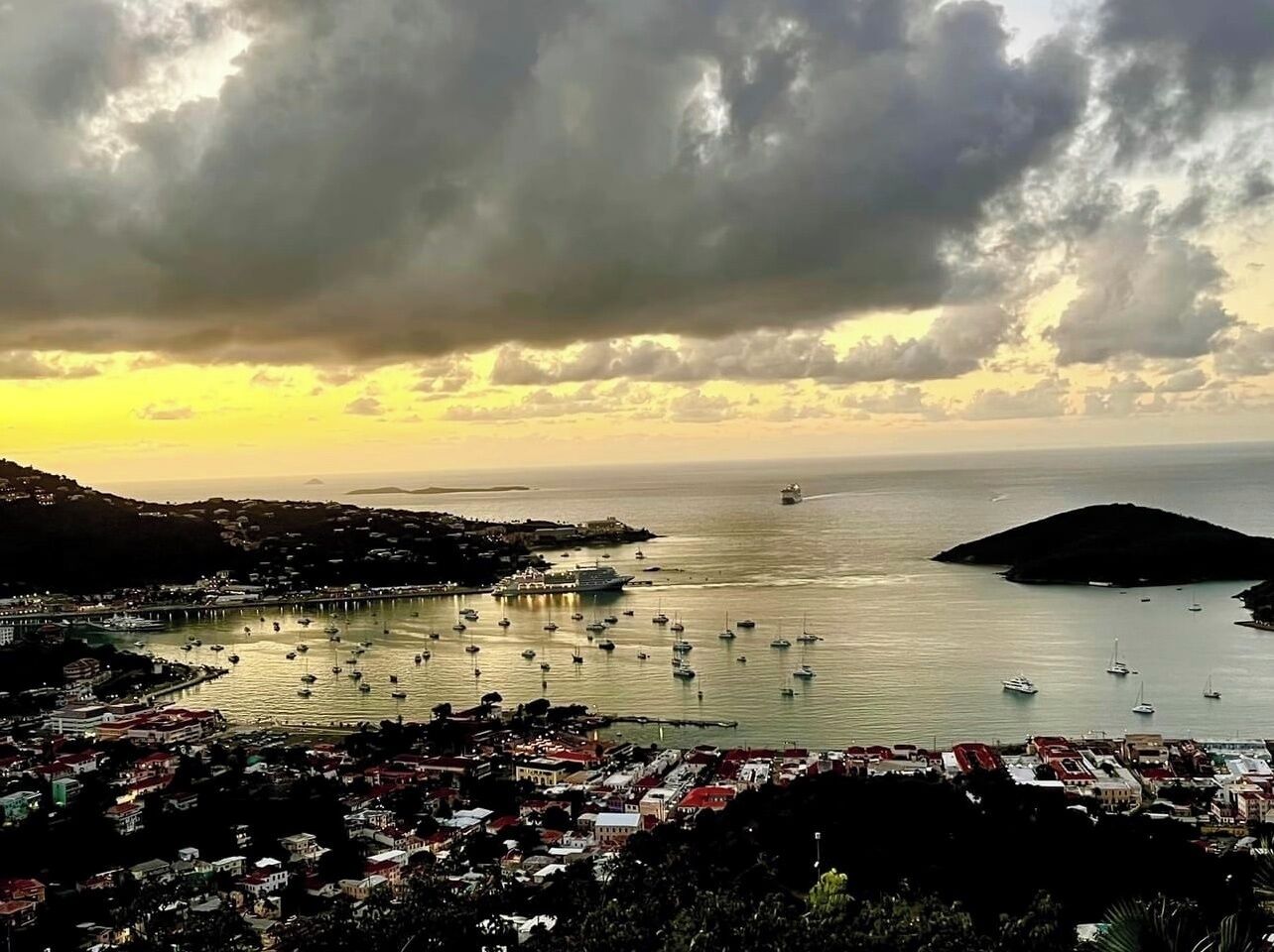 A coastal town with a marina filled with boats, a prominent ship, and a hilly landscape in the background.