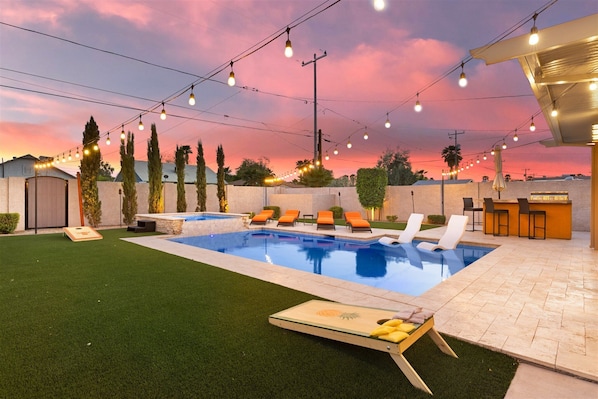 A backyard with a swimming pool, lounge chairs, and a bar area.
