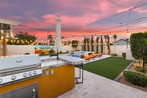 An outdoor patio with a grill, seating, and a pool.