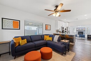 A modern living room with a sectional sofa, orange ottomans, and a ceiling fan.