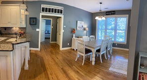 Une cuisine avec un plancher en bois, des meubles blancs et un coin repas comprenant une table et des chaises.