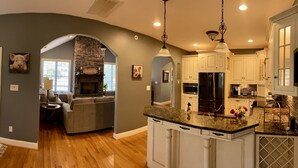 A spacious kitchen with white cabinets, a stone fireplace, and a dining area with a gray sofa. - Peaceful Mountain Home: backs to a private fishing pond on two acres (Pickens)