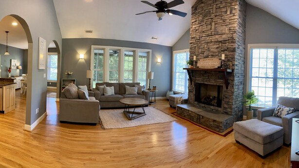 A spacious living room with a stone fireplace, large windows, and a ceiling fan. - Peaceful Mountain Home: backs to a private fishing pond on two acres (Pickens)