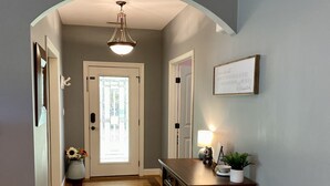A hallway with wooden flooring, a console table with a lamp, and a framed sign on the wall. - Peaceful Mountain Home: backs to a private fishing pond on two acres (Pickens)
