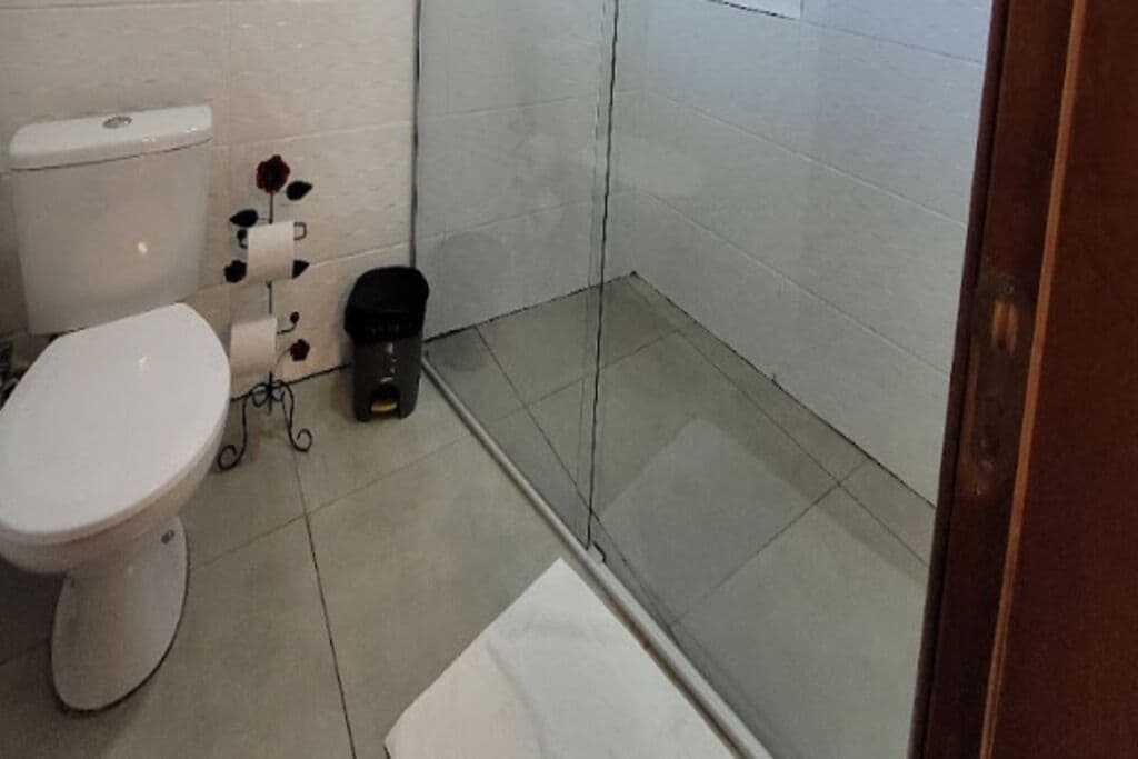 A bathroom with a toilet, a trash bin, and a shower area.
