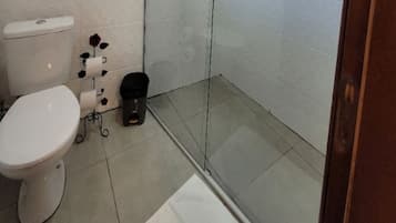 A bathroom with a toilet, a trash bin, and a shower area.