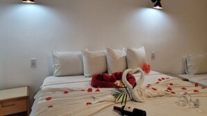A hotel room with a neatly made bed, a red heart-shaped pillow, a swan-shaped pillow, and rose petals scattered across the bed. - Pousada Sr Ivan  (Santana do Riacho)