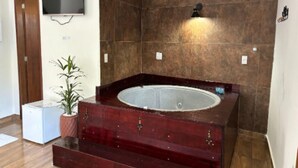 A room with a large bathtub, a television mounted on the wall, and a potted plant. - Pousada Sr Ivan  (Santana do Riacho)