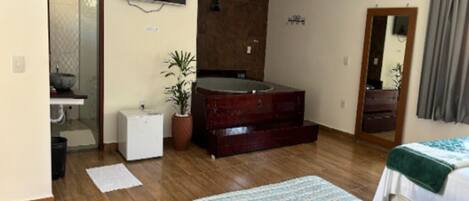 Une chambre avec un plancher en bois, un lit, une commode, un miroir et un téléviseur fixé au mur.