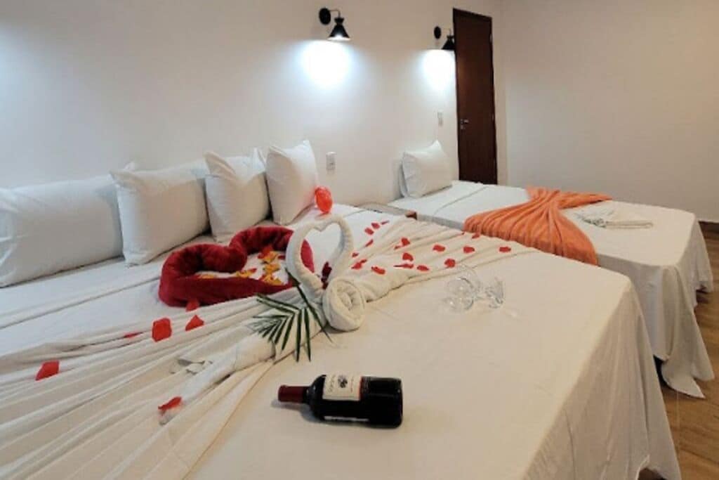 Een hotelkamer met twee bedden, witte beddengoed, een rode pluchen hoofdbord en een fles op de vloer.