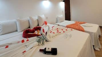 Quarto de hotel com duas camas, roupa de cama branca, cabeceira macia vermelha e uma garrafa no chão.