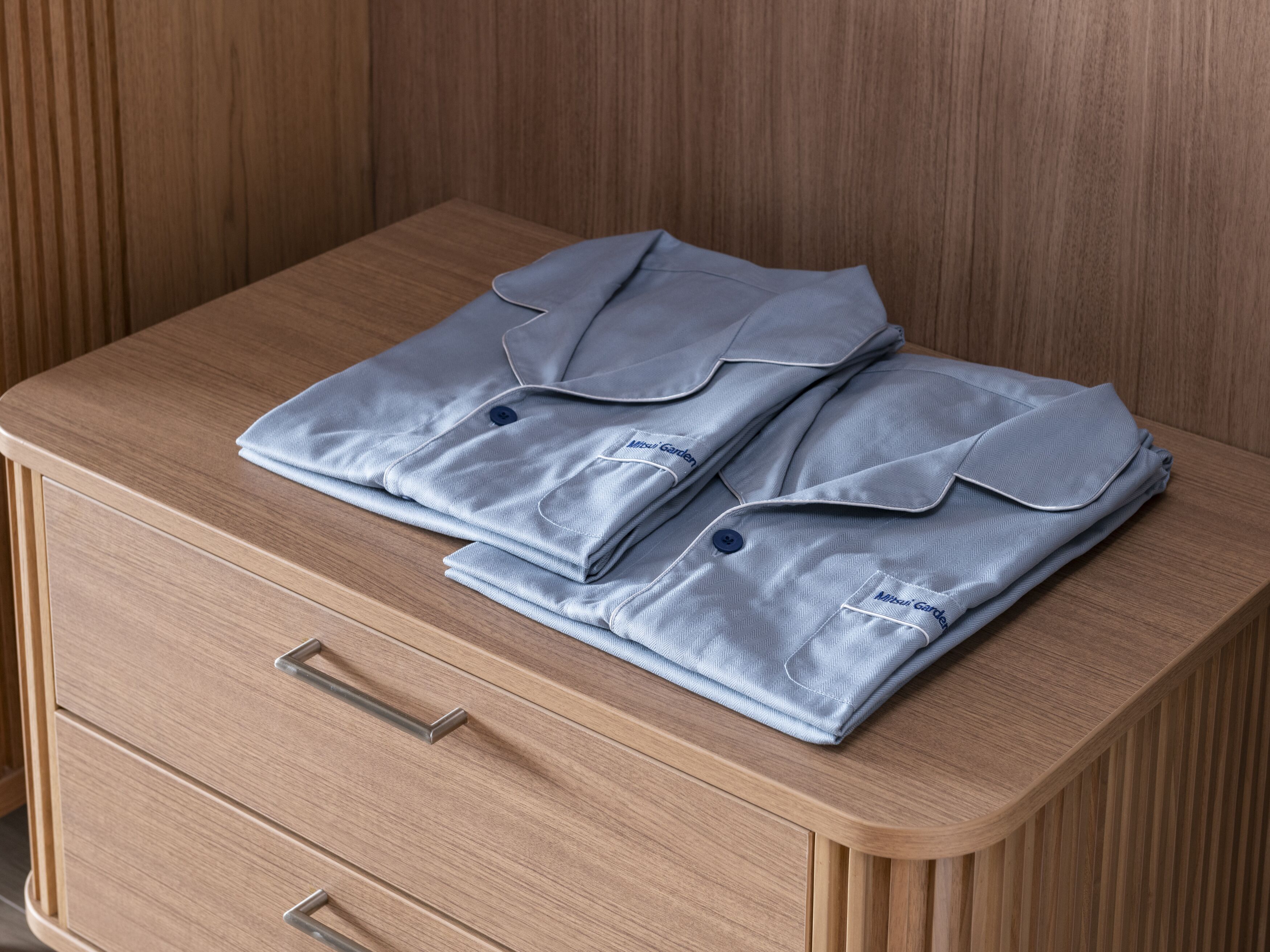 Un juego de ropa de cama azul claro, ordenadamente doblado, sobre una mesita de noche de madera con dos cajones.