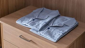 Un juego de ropa de cama azul claro, ordenadamente doblado, sobre una mesita de noche de madera con dos cajones.