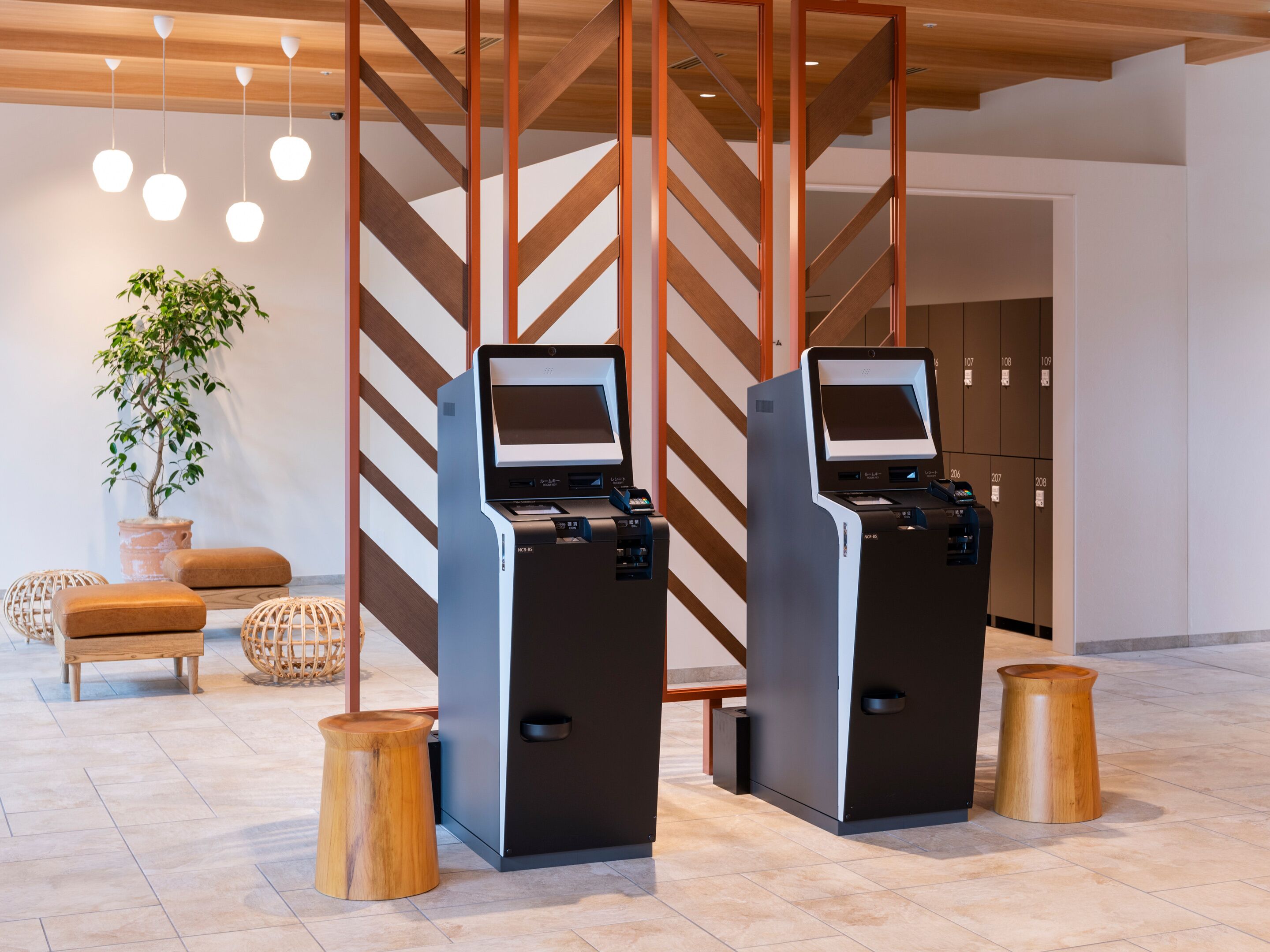 Eine moderne Lobby mit zwei Selbstbedienungskiosken, einem Topf mit Pflanze und Holzboden.