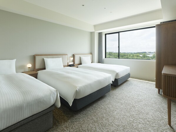 A hotel room with three beds, a large window with a city view, and a wooden cabinet. - Mitsui Garden Hotel Kashiwanoha Park Side Chiba (Kashiwa)