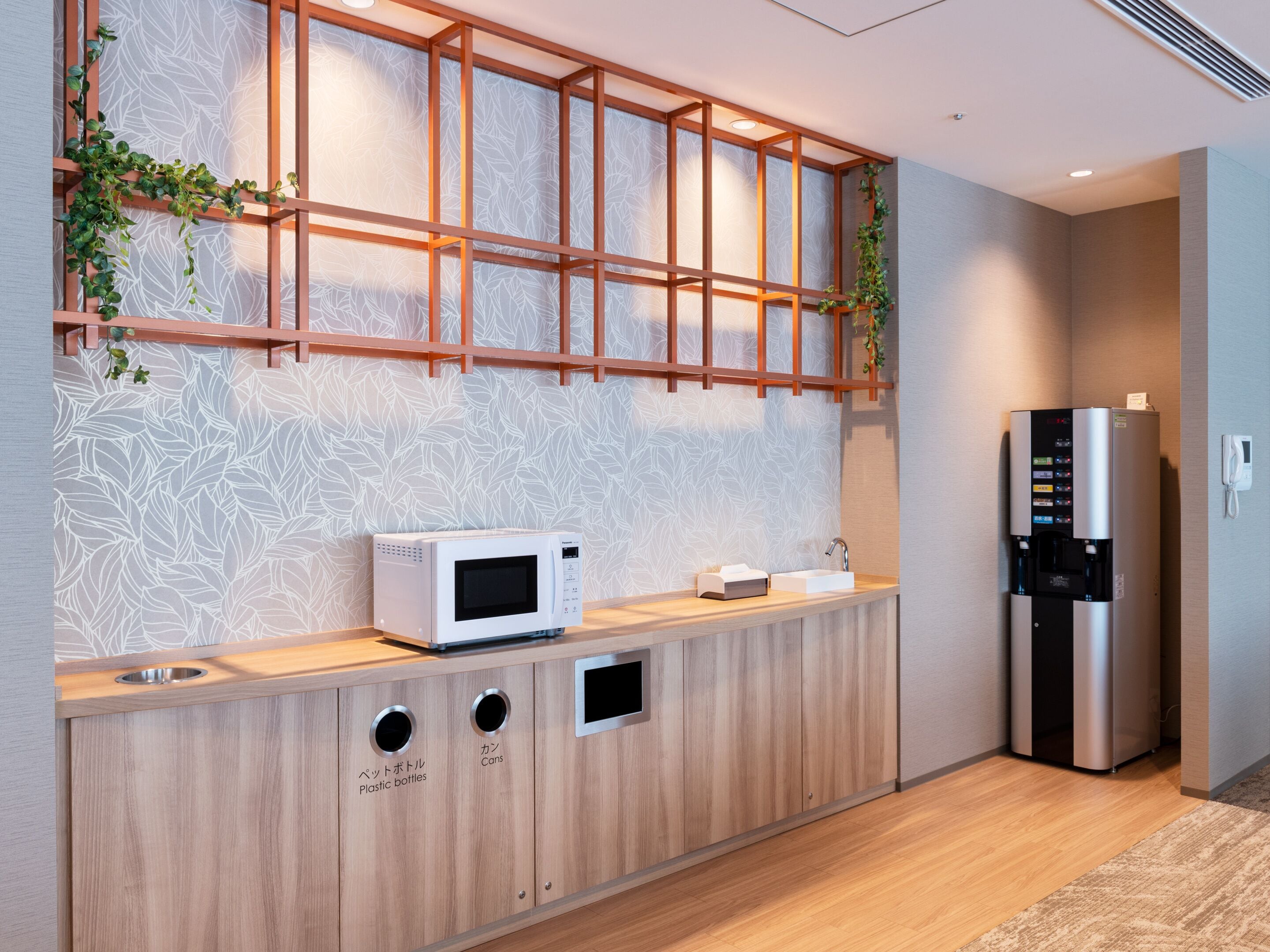 A modern kitchen with a microwave, a refrigerator, and a wooden counter with labeled compartments for plastic bottles and cans.