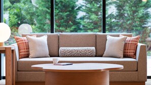 A modern living room with a sofa, patterned cushions, a round coffee table, and a view of greenery through large windows. - Mitsui Garden Hotel Kashiwanoha Park Side Chiba  (Kashiwa)