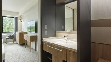 A modern bathroom with a large mirror, wooden cabinets, a sink, and a window offering a view of greenery.