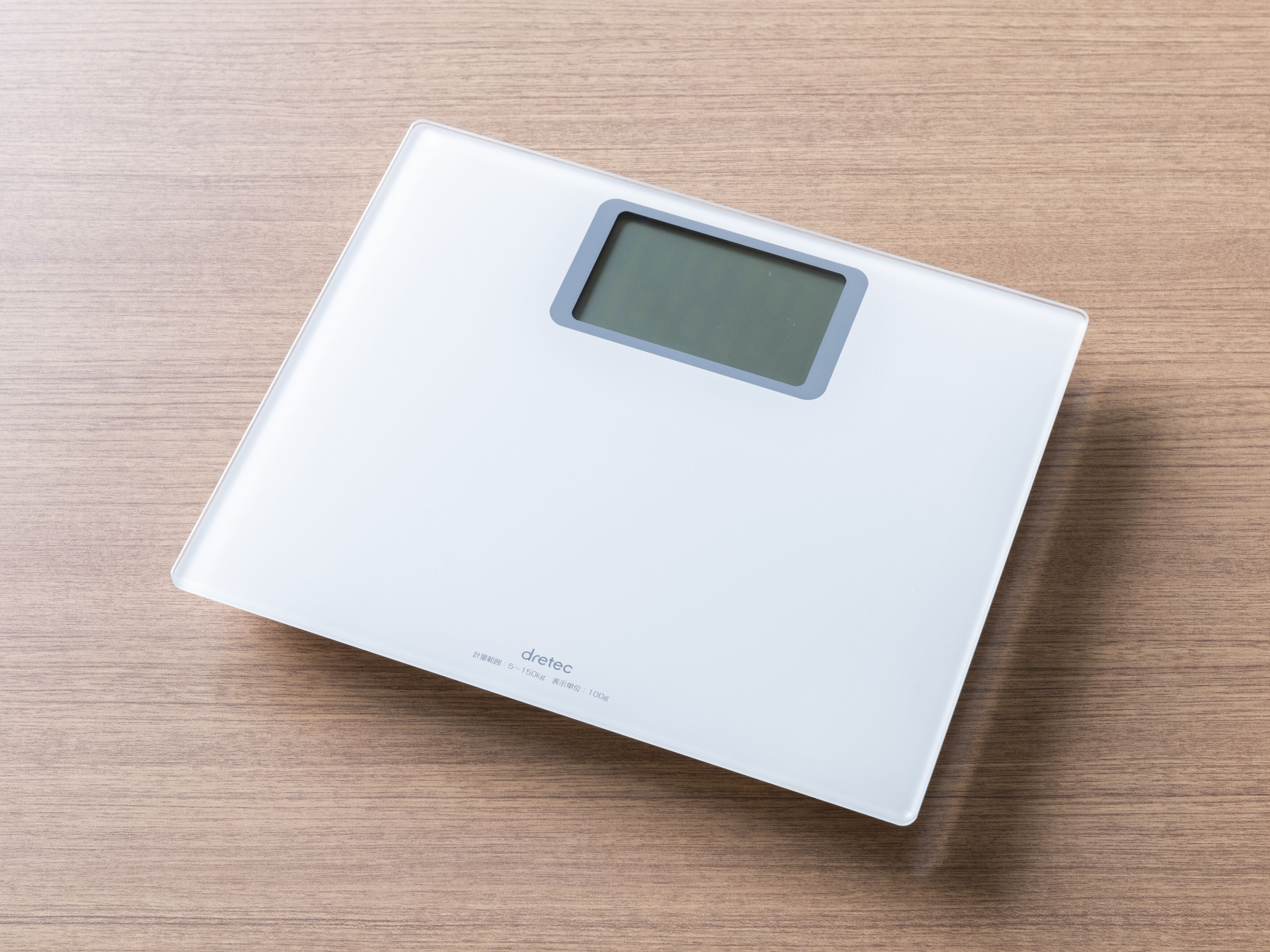 A white digital scale with a small display screen on a wooden surface.