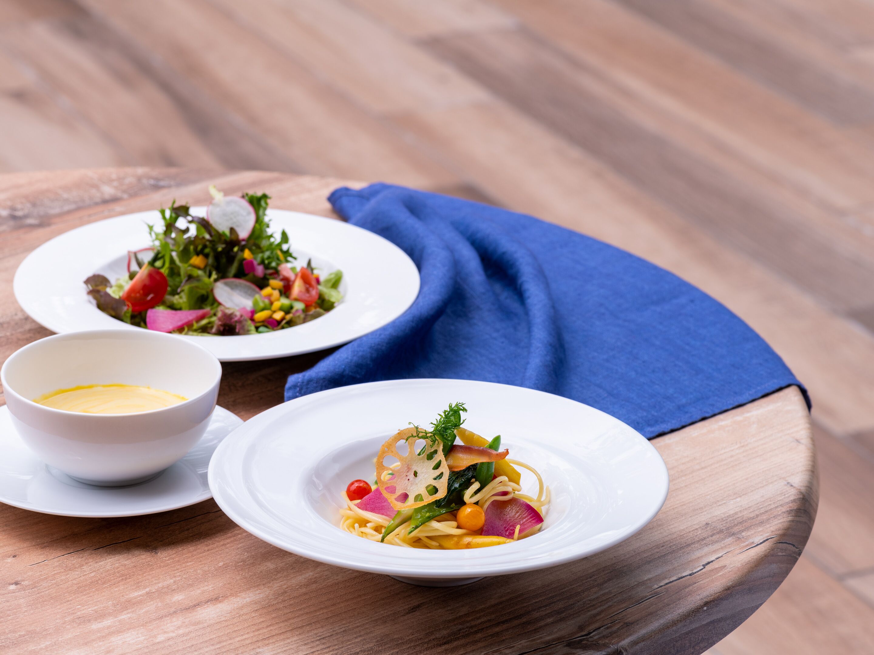 Two white plates of food on a wooden table with a blue napkin.
