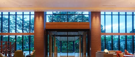 Eine großzügige Lobby mit Holzboden, großen Glasüren und moderner Möblierung.