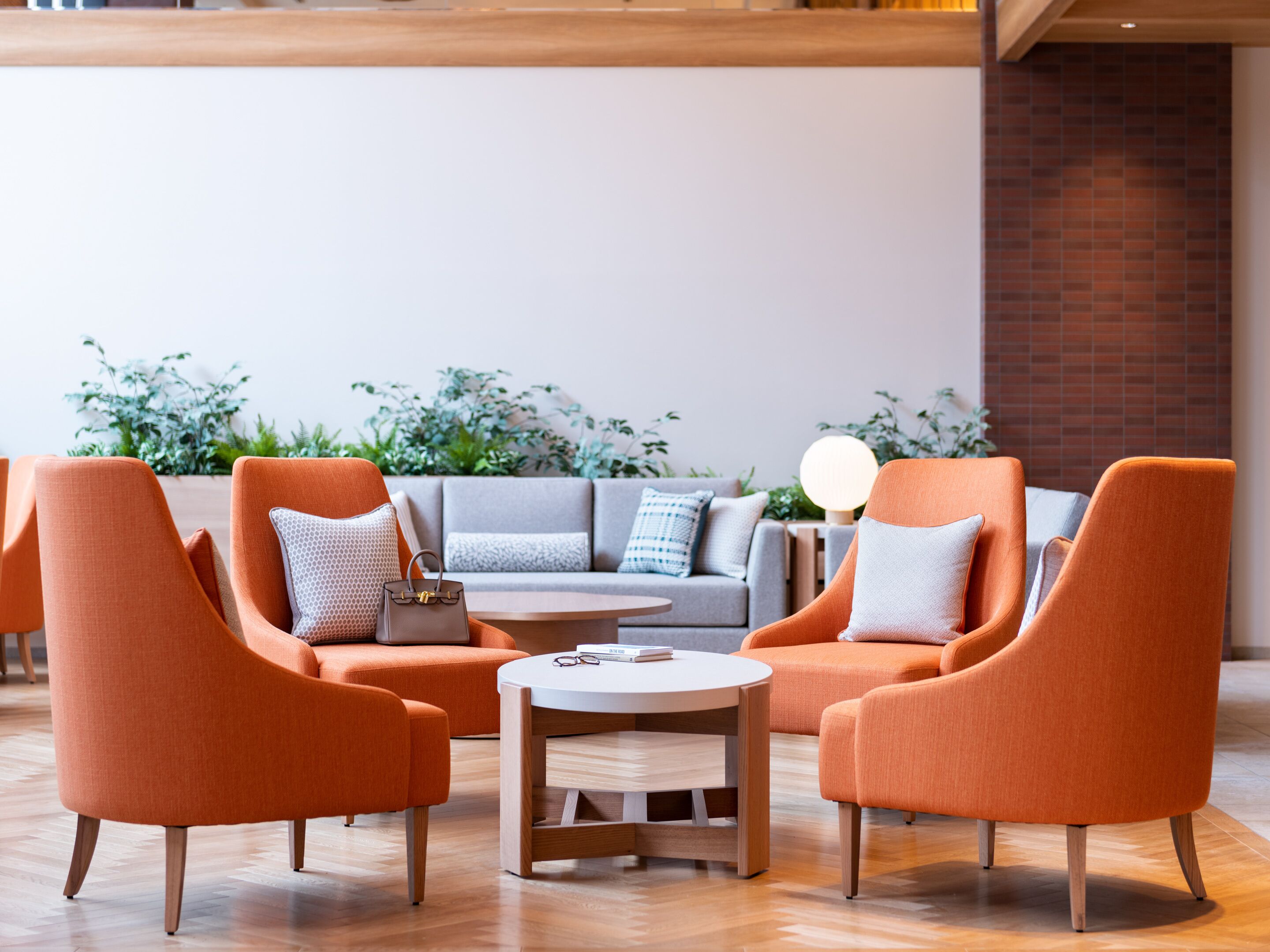 A modern lounge area with orange armchairs, a grey sofa, and a round wooden table.