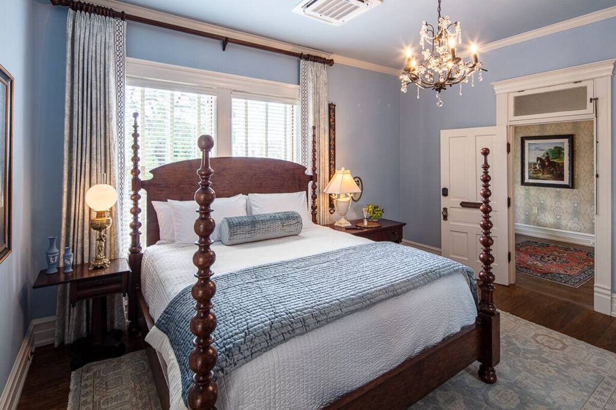 A four-poster bed with a wooden headboard, a chandelier, and a nightstand with a lamp.