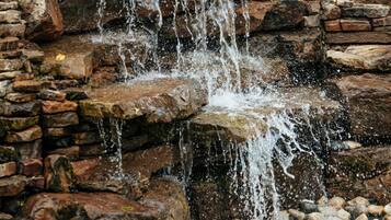 Une cascade d’eau se déversant sur une formation rocheuse et se jetant dans un bassin entouré de pierres et de galets.