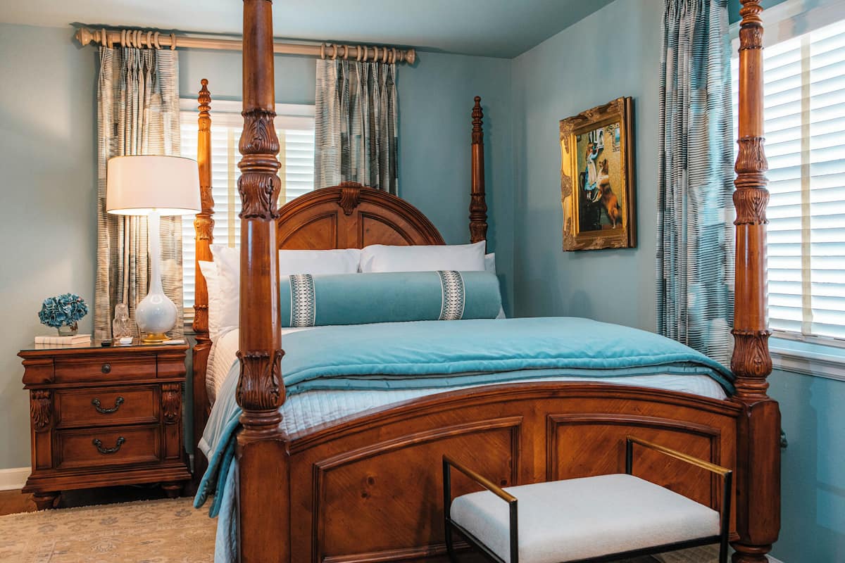 A four-poster bed with a wooden headboard, a bedside table with a lamp, and a painting on the wall.