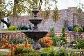 A tiered stone fountain in a garden with brick walls and a metal fence in the background. - The Reserve at Hot Springs (Hot Springs)