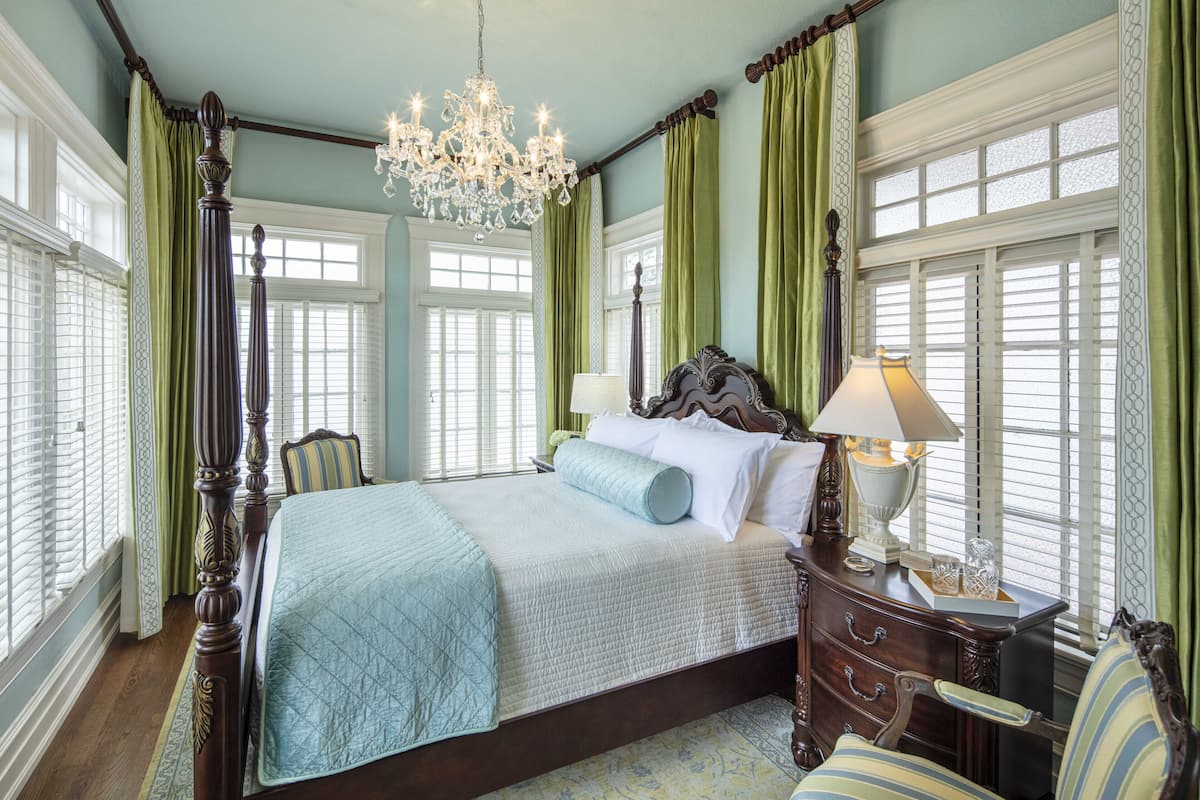 A bedroom with a four-poster bed, a chandelier, and green curtains.