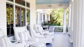 A covered porch with white wicker furniture and columns. - The Reserve at Hot Springs (Hot Springs)