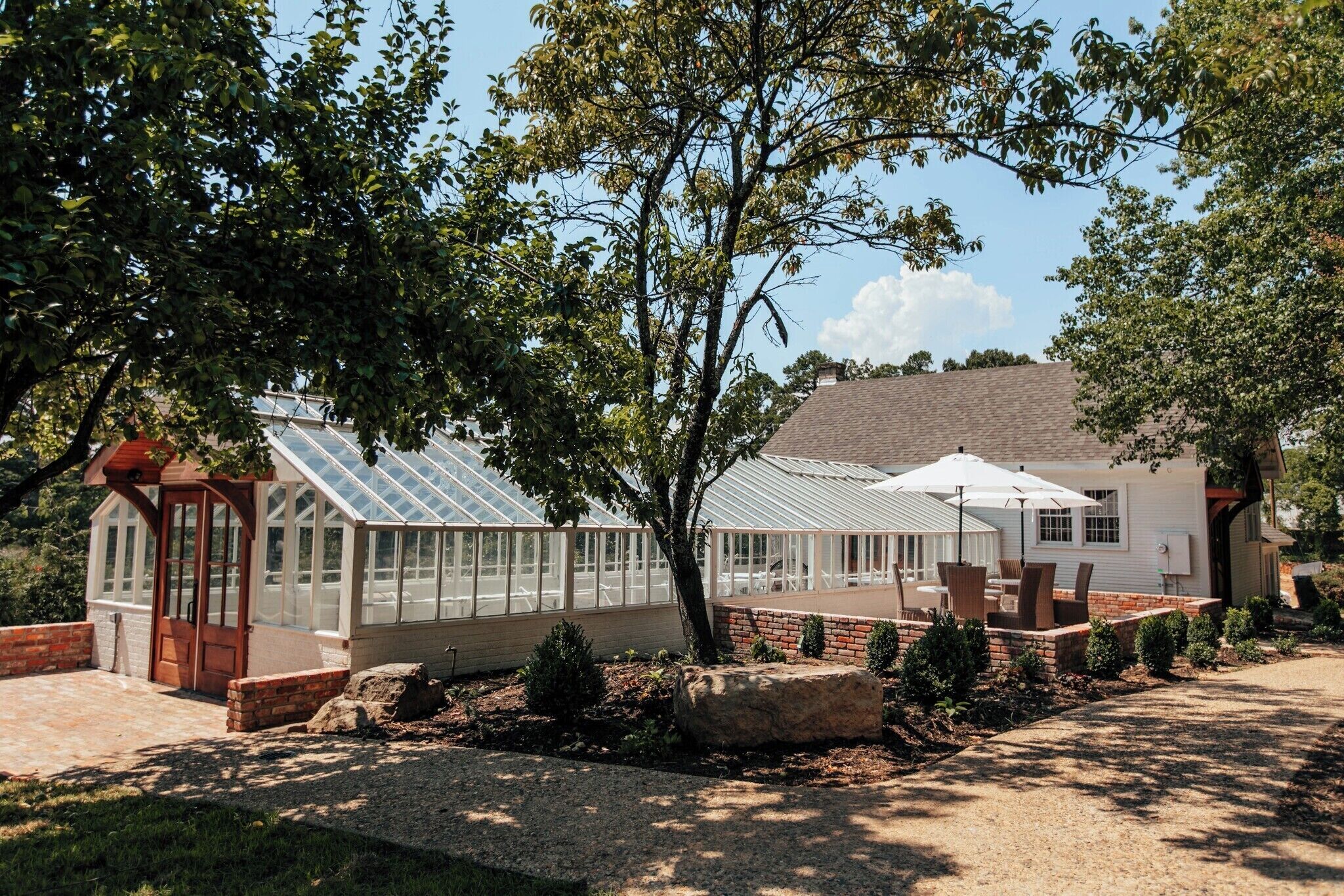 A greenhouse with a glass roof, surrounded by a brick patio and a gravel path.