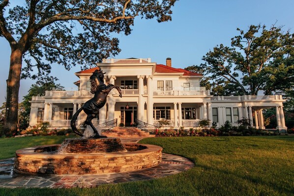 A stately white building with a red roof, a fountain with a horse statue, and a large tree in the foreground. - The Reserve at Hot Springs (Hot Springs)